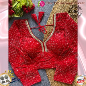 Pode incluir: Uma blusa vermelha de manga comprida com bordados dourados intrincados e um decote em V profundo. A blusa apresenta um padrão decorativo e acabamentos dourados ao longo do decote. O texto "The Traditional Street" é visível.