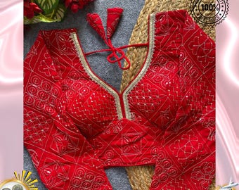 May include: A red long-sleeved blouse with intricate gold embroidery and a deep V-neckline. The blouse features a decorative pattern and gold trim along the neckline. The text "The Traditional Street" is visible in the image.