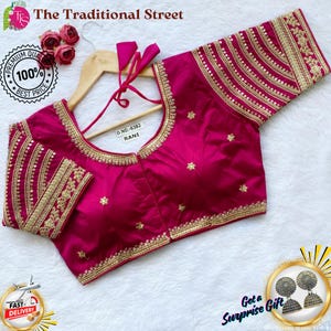 Pode incluir: Uma blusa magenta com bordados dourados e detalhes de lantejoulas. A blusa apresenta um decote redondo e mangas até o cotovelo. O texto "The Traditional Street" está no topo. O texto "RANI" é visível. A blusa é exibida em um cabide de madeira.