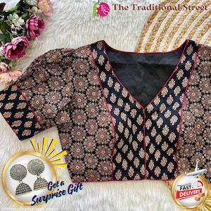 May include: A black blouse with a V-neck and short sleeves. The blouse features a repeating pattern of brown and gold floral designs. The neckline and sleeve edges are trimmed with a thin red border. The image also includes a pair of silver earrings.