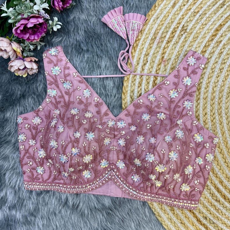 May include: A pink sleeveless blouse with a V-neckline and floral embroidery. The blouse is decorated with sequins and beads.