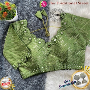 Pode incluir: Uma blusa verde com intrincados enfeites de espelho e lantejoulas. A blusa apresenta um decote e mangas com vieiras, com um fecho de laço. The Traditional Street é impresso no topo. Uma entrega rápida e um distintivo de presente surpresa também são visíveis.