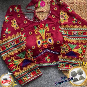 Pode incluir: Uma blusa bordô com bordados intrincados em amarelo, verde, azul e vermelho. A blusa tem mangas compridas e decote redondo. O texto "The Traditional Street" é visível.
