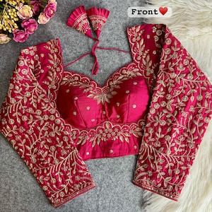 Puede incluir: Una blusa magenta con mangas largas y bordados dorados intrincados. La blusa presenta un escote de corazón y está adornada con patrones florales y de hojas. La palabra "Front" es visible en la parte superior, junto con un símbolo de corazón.