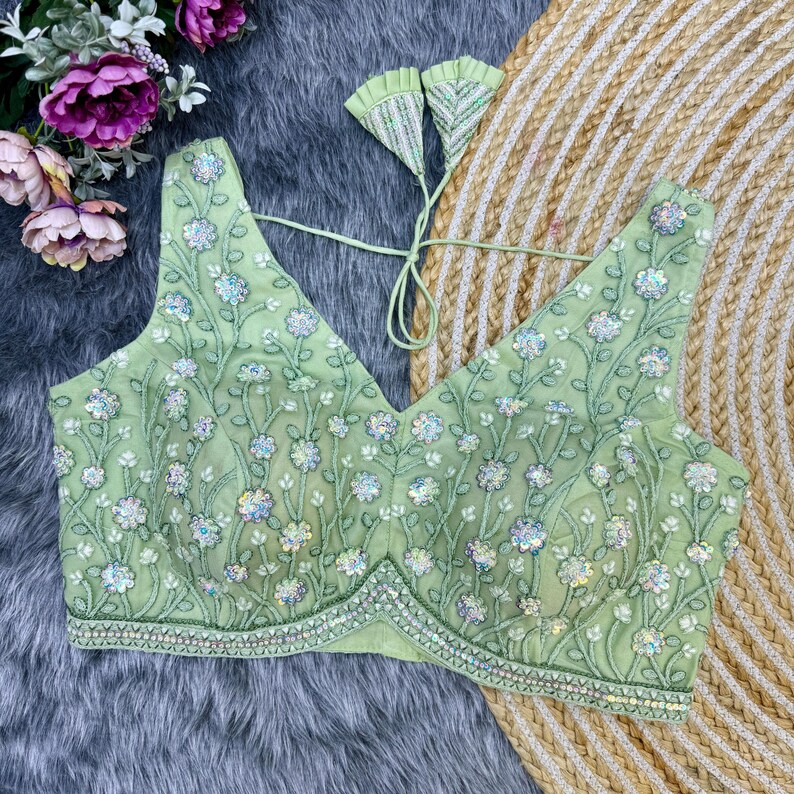 May include: A light green embroidered blouse with a V-neckline and a floral pattern. The blouse is decorated with sequins and beads.