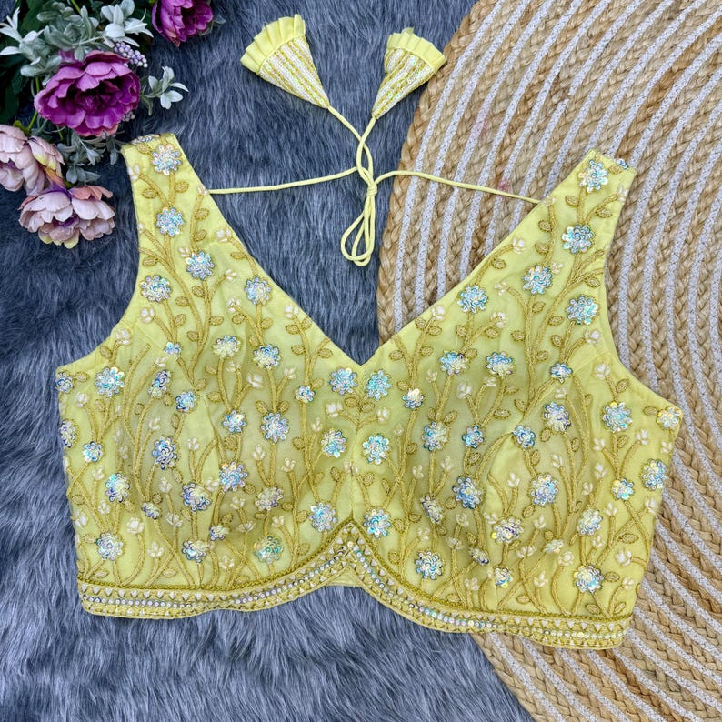May include: A yellow embroidered blouse with a V-neckline and sleeveless design. The blouse is decorated with floral patterns and sequins.