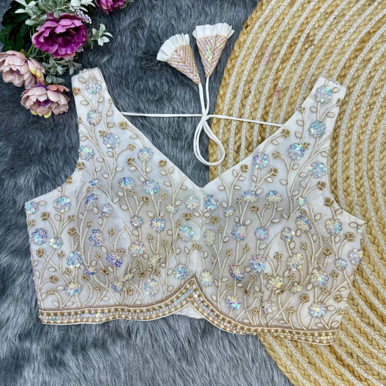 May include: White embroidered blouse with a V-neckline and a floral design. The blouse is decorated with sequins and beads.