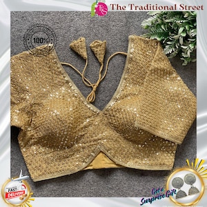 Pode incluir: Blusa dourada com lantejoulas, decote em V profundo e mangas curtas. A blusa apresenta detalhes intrincados de lantejoulas e uma borda ondulada. O logotipo The Traditional Street é visível.