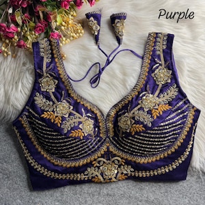 Puede incluir: Una blusa morada sin mangas con intrincados bordados dorados, detalles de lentejuelas y un escote corazón. La prenda incluye dos lazos de tela morada a juego con adornos en tono dorado en los extremos. El texto "Purple" es visible.