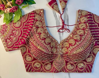 Può includere: Una camicetta magenta con intricati ricami dorati in motivi paisley e floreali, maniche corte, una scollatura profonda e due nappe in tessuto magenta abbinate con decorazioni dorate attaccate sul retro con sottili cordini rossi.