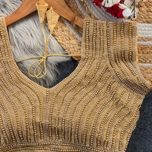 Pu&ograve; includere: Una blusa dorata senza maniche con un profondo scollo a V e intricate file verticali di perline e strass scintillanti. Il capo presenta sottili lacci in tessuto dorato sul retro con estremit&agrave; appuntite e un aspetto strutturato.