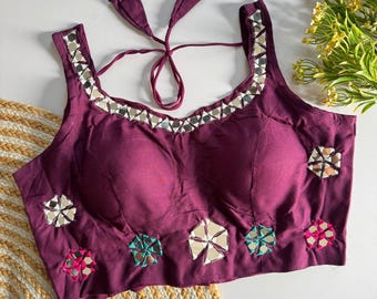 May include: A deep purple sleeveless blouse featuring a square neckline adorned with a border of small reflective mirror pieces. The garment includes tie-back straps and is decorated with scattered floral-shaped mirror embellishments.