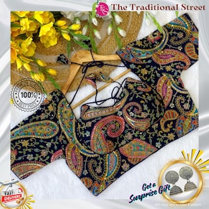 Pode incluir: Uma blusa azul marinho com estampa paisley com bordados e enfeites intrincados. A blusa é exibida em um cabide de madeira, mostrando seu design detalhado e cores vibrantes. A imagem inclui o texto "The Traditional Street".