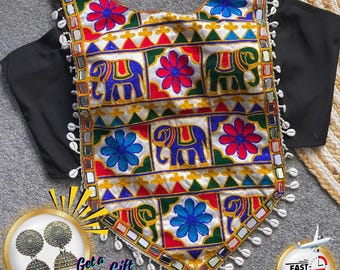 May include: A colorful embroidered top with elephant and floral patterns. The top features a white base with red, blue, and green accents. The edges are adorned with small mirrors and white shells. Black sleeves are attached to the top.