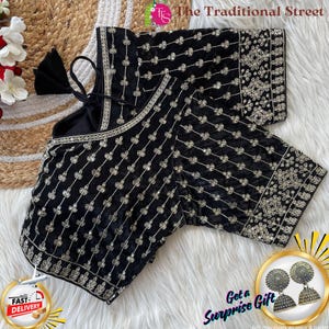 Pode incluir: Blusa de veludo preto com bordados prateados intrincados. A blusa apresenta um decote redondo e mangas compridas. O logótipo The Traditional Street é visível. A blusa é exibida numa superfície branca e fofa.