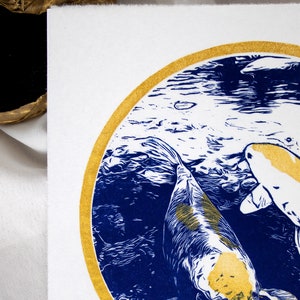 May include: A blue and gold print of two koi fish swimming in a circle. The fish are white with gold accents and are swimming in a blue and white water pattern.
