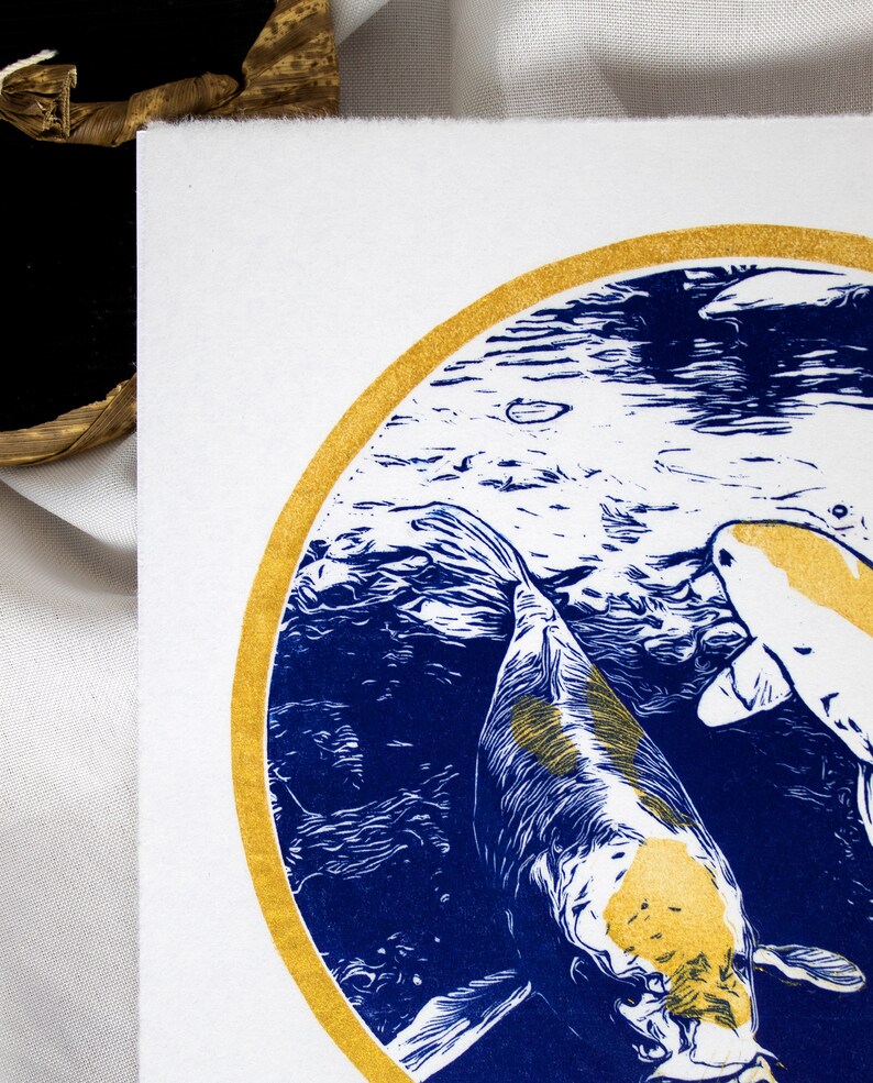 May include: A blue and gold print of two koi fish swimming in a circle. The fish are white with gold accents and are swimming in a blue and white water pattern.
