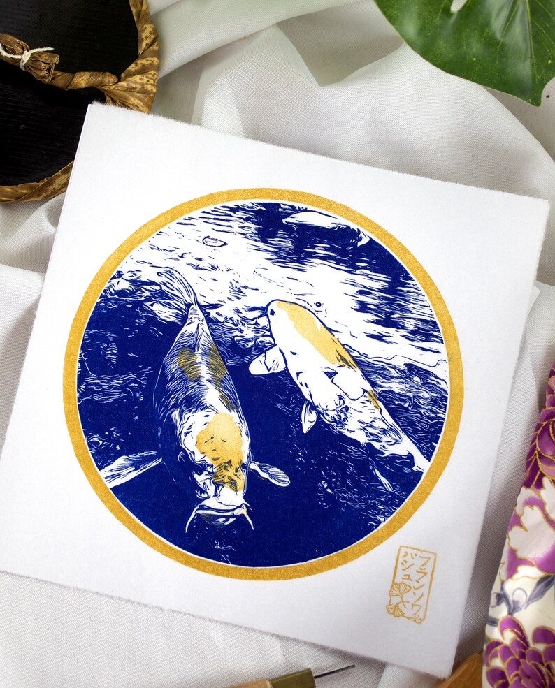 May include: A gold and blue print of two koi fish swimming in a circle. The print is on a white background and has a gold border. The artist's signature is in the bottom right corner.