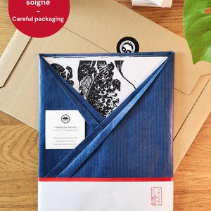 May include: A blue and white envelope with a red stripe and a white label that says "Emballage soign&eacute; - Careful packaging". The envelope is wrapped around a white piece of paper with a black and white illustration of a Japanese woodblock print.