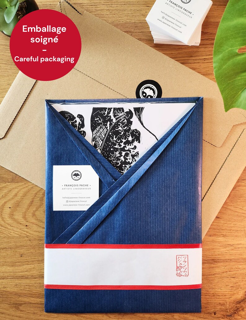 May include: A blue and white envelope with a red stripe and a white label that says "Emballage soign&eacute; - Careful packaging". The envelope is wrapped around a white piece of paper with a black and white illustration of a Japanese woodblock print.