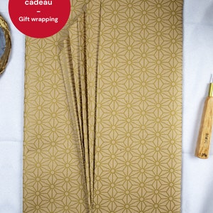 May include: A stack of brown gift wrapping paper with a gold geometric pattern. The paper is folded in a fan shape and has the text "Emballage cadeau - Gift wrapping" printed on the top sheet.