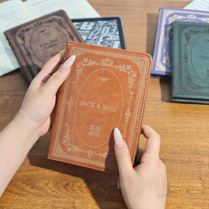 Puede incluir: Una funda de libro de cuero marr&oacute;n con el texto "JACK & ROSE" en letras doradas. La funda tiene un dise&ntilde;o ornamental en los bordes y un peque&ntilde;o c&oacute;digo QR. Se ven otras fundas de libros, incluida una con el texto "Hot Girl Reads".