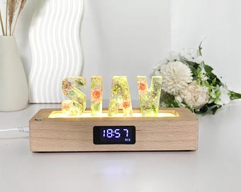 May include: A wooden base with the letters S, H, A, and Y, each filled with colorful flowers and greenery. The base has a digital clock displaying 18:57. The letters are illuminated with a warm glow.