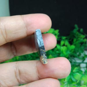 Puede incluir: Una piedra preciosa pulida con una mezcla de colores, incluyendo gris, negro y marr&oacute;n. La piedra tiene un patr&oacute;n y una textura &uacute;nicos, y se sostiene en la mano de una persona.