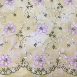 Pode incluir: Um tecido transparente com um delicado padrão de bordado floral. As flores são de cor lilás claro e os caules são de cor verde escuro. O tecido tem um brilho sutil.