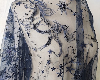 May include: Navy blue tulle fabric with an embroidered design. The design features a prancing horse, stars, and beaded accents. The horse and stars are in shades of blue, creating a celestial theme. The fabric is semi-sheer and suitable for apparel or decorative projects.