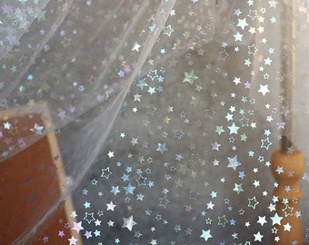 May include: Sheer white fabric with scattered iridescent star shapes. The stars reflect a range of colors, including silver, blue, and purple. The fabric appears delicate and lightweight, suitable for decorative purposes.