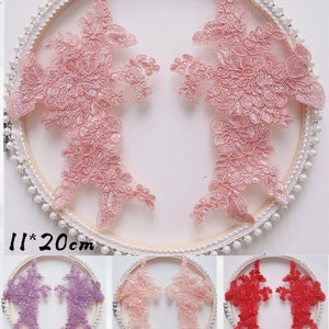 May include: Two pink floral lace appliques, each measuring 11 inches by 20 inches, displayed on a white background. The appliques are in the shape of a stylized flower with intricate details. The appliques are shown in three different colors: pink, purple, and red.