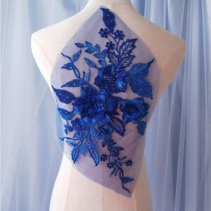 Könnte beinhalten: Königsblaue Blumenapplikation mit Pailletten und Perlen auf einem durchsichtigen Netzstoff. Diese zarte Verzierung ist perfekt, um Kleidung, Accessoires oder Heimtextilien einen Hauch von Eleganz zu verleihen.