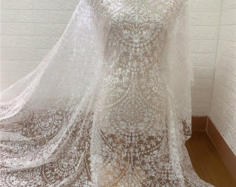 May include: White lace fabric with a delicate floral pattern. The lace is sheer and has a soft, flowing texture.