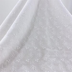 May include: White cotton fabric with a delicate embroidered floral pattern. The fabric has a soft, airy feel and is perfect for crafting projects.