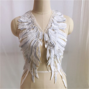 May include: White lace applique with a delicate, feathered design. The applique is shaped like a pair of wings and is perfect for adding a touch of elegance to any garment.