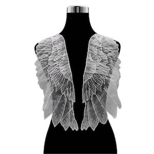 May include: White lace angel wings with a delicate, intricate design. The wings are attached to a black mannequin, creating a dramatic and ethereal look.
