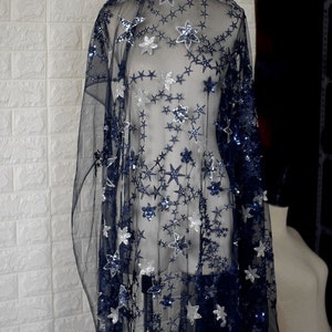 May include: Black sheer fabric with silver and blue star-shaped sequins. The fabric is draped over a dress form.