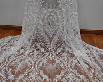 Puede incluir: Tela de encaje blanca con cuentas con un patrón floral. La tela está adornada con lentejuelas y cuentas.