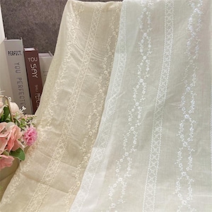 May include: Two pieces of white fabric with embroidered floral patterns. The fabric on the left is a light beige color, while the fabric on the right is a bright white.