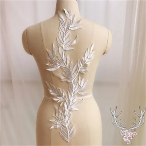 May include: White lace applique with a leafy design. The applique is on a white mannequin.