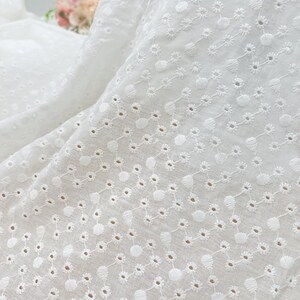 May include: White cotton fabric with a delicate eyelet pattern. The fabric has a subtle sheen and a soft, airy feel.