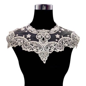 Puede incluir: Collar de encaje blanco con borde festoneado y diseño floral. El collar se muestra en un maniquí negro.