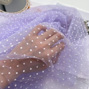 May include: Purple sheer fabric with white polka dots. The fabric is soft and delicate, ideal for crafting or sewing.