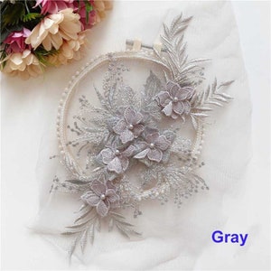 May include: A silver and gray floral applique with pearl accents. The applique is on a white background and is surrounded by a hoop.