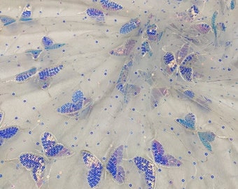 May include: White sheer fabric with iridescent blue butterfly sequins. The butterflies are scattered randomly across the fabric.