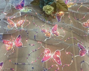 May include: A sheer white fabric with pink and purple butterfly sequins. The fabric is decorated with small iridescent beads.