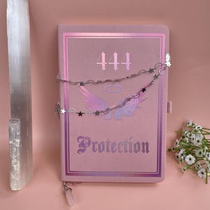 May include: A pink journal with the number 444 and the word "Protection" printed on the cover. The journal is decorated with a silver chain with star charms and a clear crystal pendant.