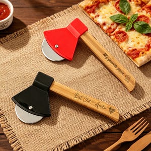 May include: Two pizza cutters shaped like axes with wooden handles and circular stainless steel blades. One handle features the text "My favourite pizza" with a slice icon, while the other displays "Best Chef - Amelia" with a heart icon.