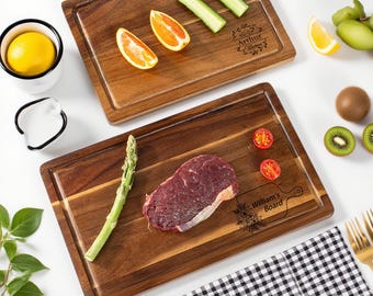 May include: Two rectangular wooden cutting boards with a juice groove. One board has orange slices and cucumber, the other has a steak, asparagus, and tomatoes. One board is labeled "Arthur's Kitchen", the other "William's Board".